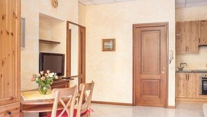 Une pièce comprenant une table à manger en bois, des chaises, un téléviseur, un coin cuisine avec des placards en bois et une porte.