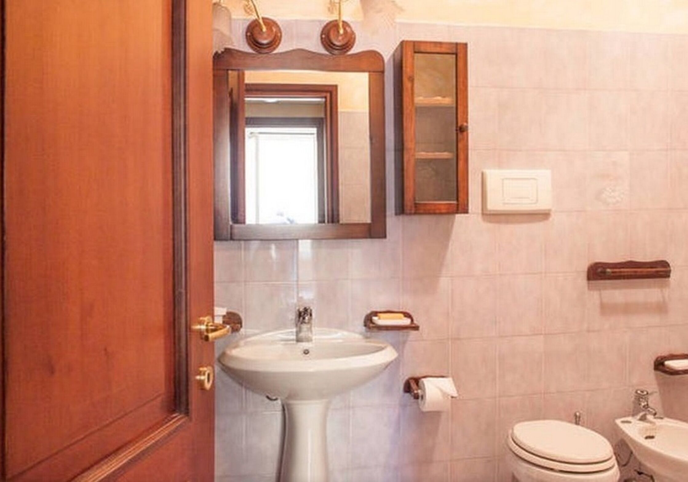 A bathroom with a pedestal sink, a toilet, a mirror, and a cabinet.