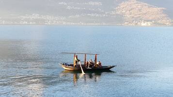 Un bateau transportant des passagers sur une étendue d’eau calme, entouré d’une côte lointaine parsemée de bâtiments.
