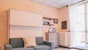 Une pièce avec un canapé gris, un meuble, un radiateur et une fenêtre avec des rideaux.