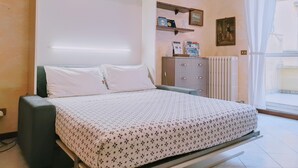 Une chambre à coucher avec un lit, une commode, un radiateur et une fenêtre avec des rideaux.