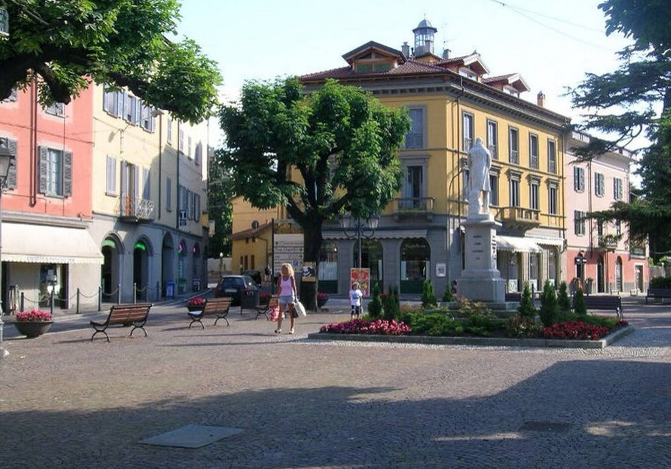 A cobblestone square with benches, a statue, and historic buildings.