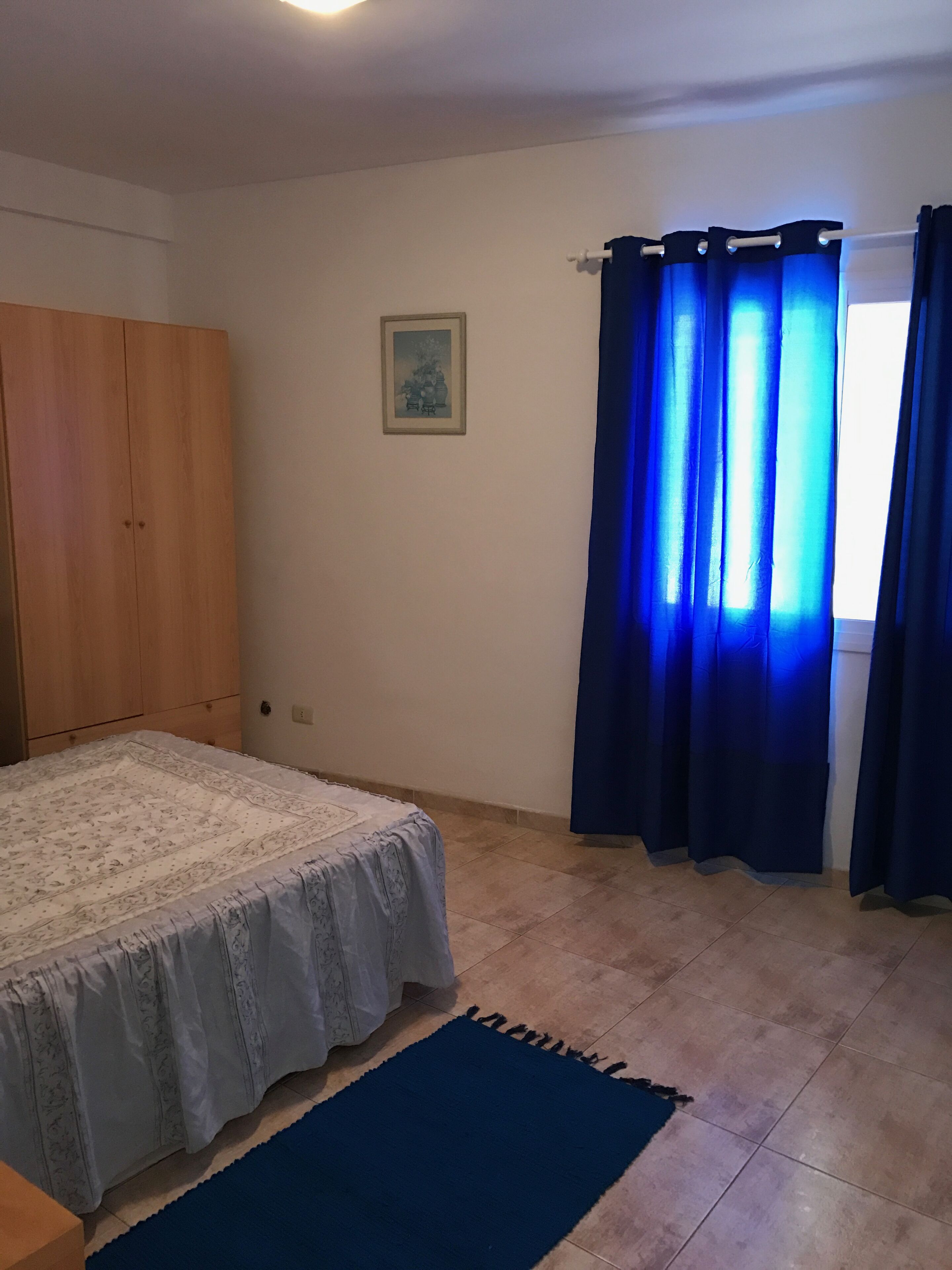 Una camera da letto con un letto, un armadio, un quadro appeso alla parete e una finestra con tende blu.