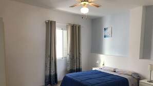 A bedroom with a bed, a nightstand, a lamp, a ceiling fan, and a window with curtains. - Front line apartment in Puerto Santiago-Los Gigantes with beautiful views.<br> (Puerto Santiago)