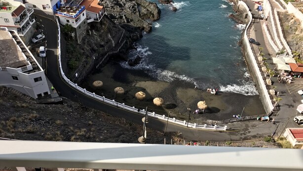 A coastal road with a bridge leading to a beach area with umbrellas and a rocky shoreline. - Front line apartment in Puerto Santiago-Los Gigantes with beautiful views.<br> (Puerto Santiago)