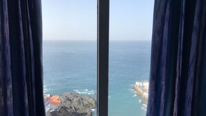 A view through a window with curtains, featuring a coastal landscape with rocky outcrops and a building with a red roof. - Front line apartment in Puerto Santiago-Los Gigantes with beautiful views.<br> (Puerto Santiago)