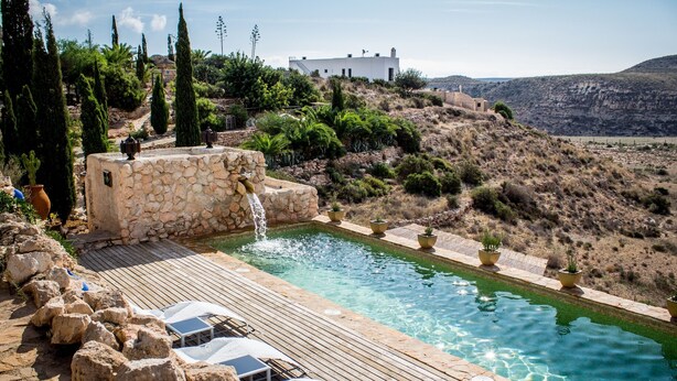 A pool area with a stone wall, a waterfall feature, and lounge chairs. - La Joya de Cabo de Gata - Cortijo El Cala Plomo (Agua Amarga)
