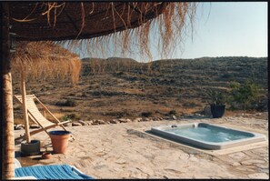 Relax in a serene outdoor setting with a hot tub, lounge chair, and shaded area.
