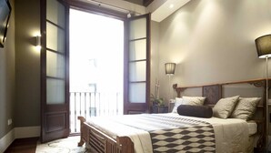 A bedroom with a bed, a nightstand, a lamp, and a view of the outside.