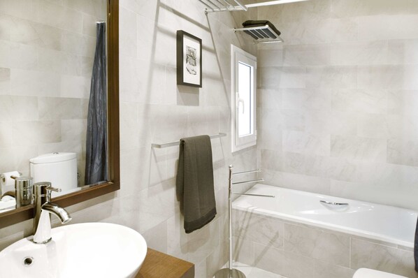 Un baño con un lavabo blanco, un espejo, un perchero para toallas, un inodoro y una bañera.
