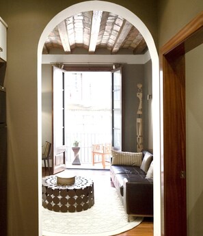 Un interior con un sofá, un taburete estampado y vistas a un balcón exterior a través de un arco.