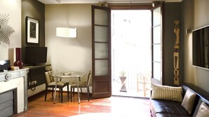 A room with a dining table and chairs, a sofa, a television, and a large window with a view of the outside.