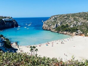 A coastal beach with clear turquoise waters, a sandy shore, and a rocky cliff.