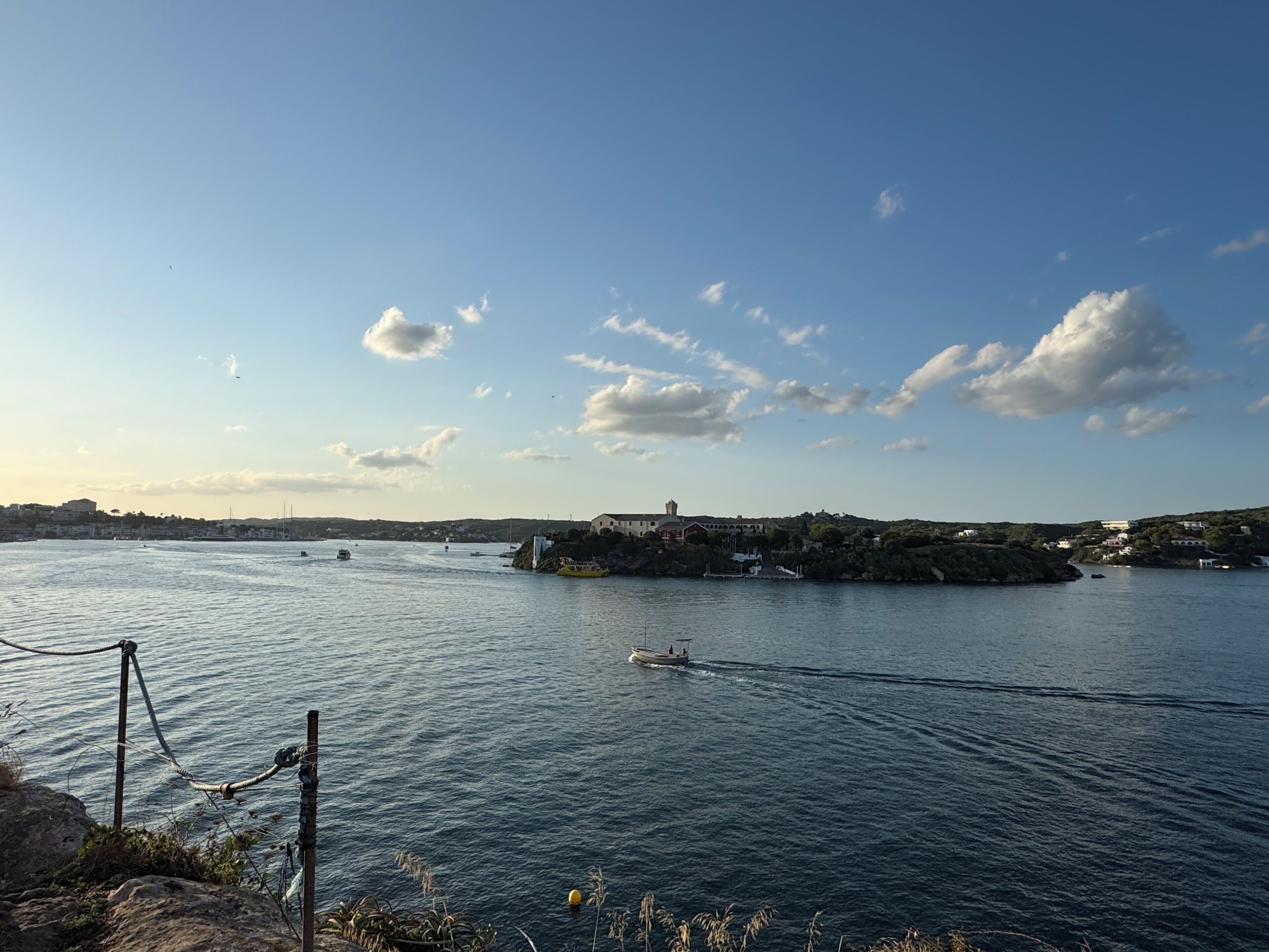 A coastal view with a body of water, boats, and a distant building complex.