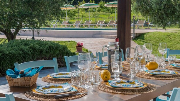 An outdoor dining area with a table set for a meal, surrounded by chairs and umbrellas. - Villa Rosa - Private villa, 5 bedrooms, pool, A/C, wifi, pets, Marche (Fossombrone)