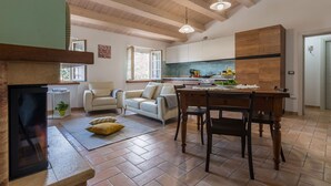 A spacious living area with a fireplace, a dining table with chairs, a kitchen with modern appliances, and a large window providing natural light. - Villa Rosa - Private villa, 5 bedrooms, pool, A/C, wifi, pets, Marche (Fossombrone)
