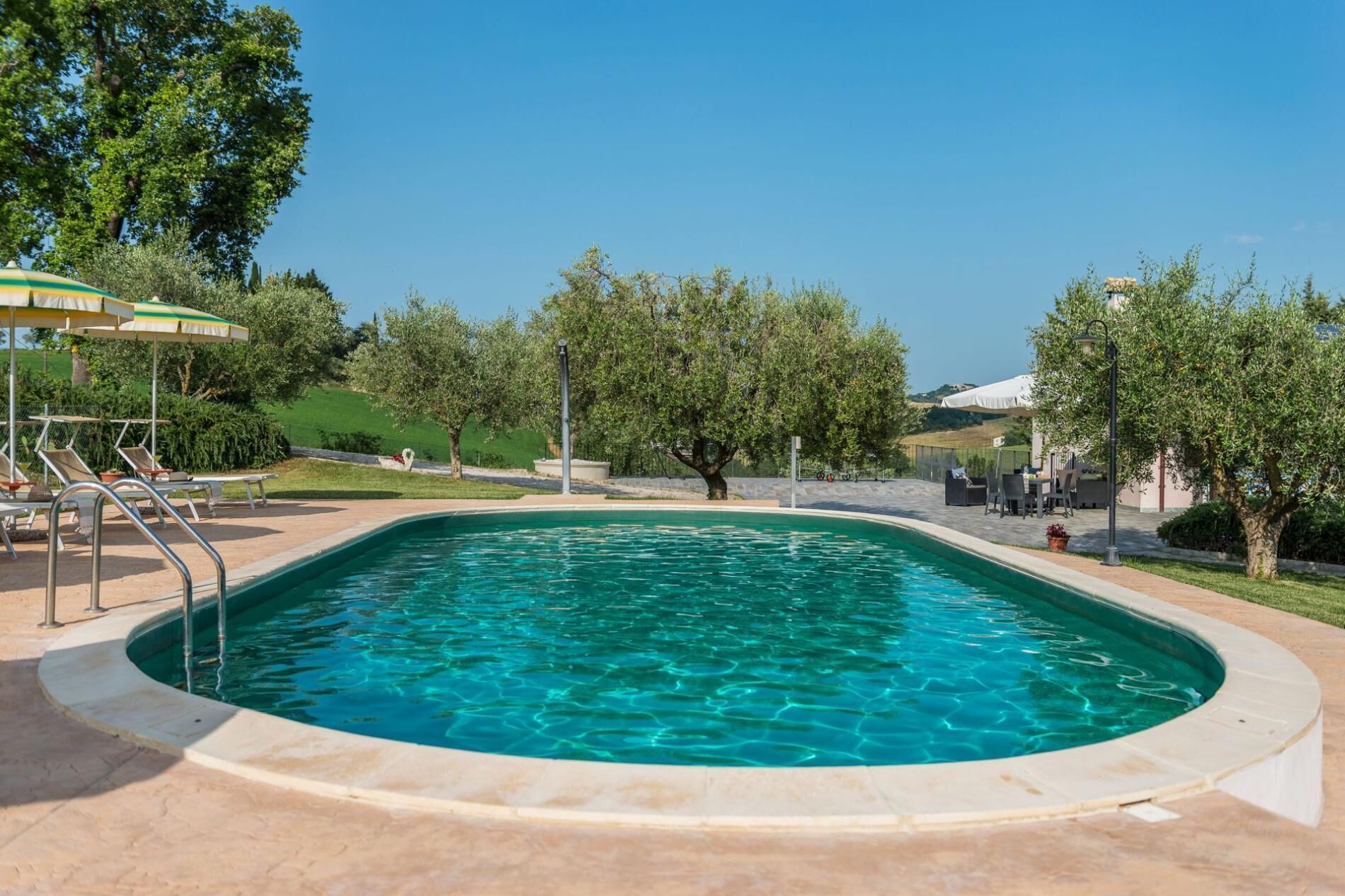 A swimming pool with a curved edge, surrounded by lounge chairs and umbrellas.