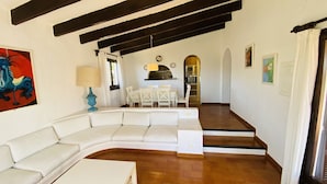 Ein Wohnzimmer mit weißem Sofa, einem Esstisch mit Stühlen, einer Küchenzeile mit Geräten und einer Treppe zu einer weiteren Ebene.