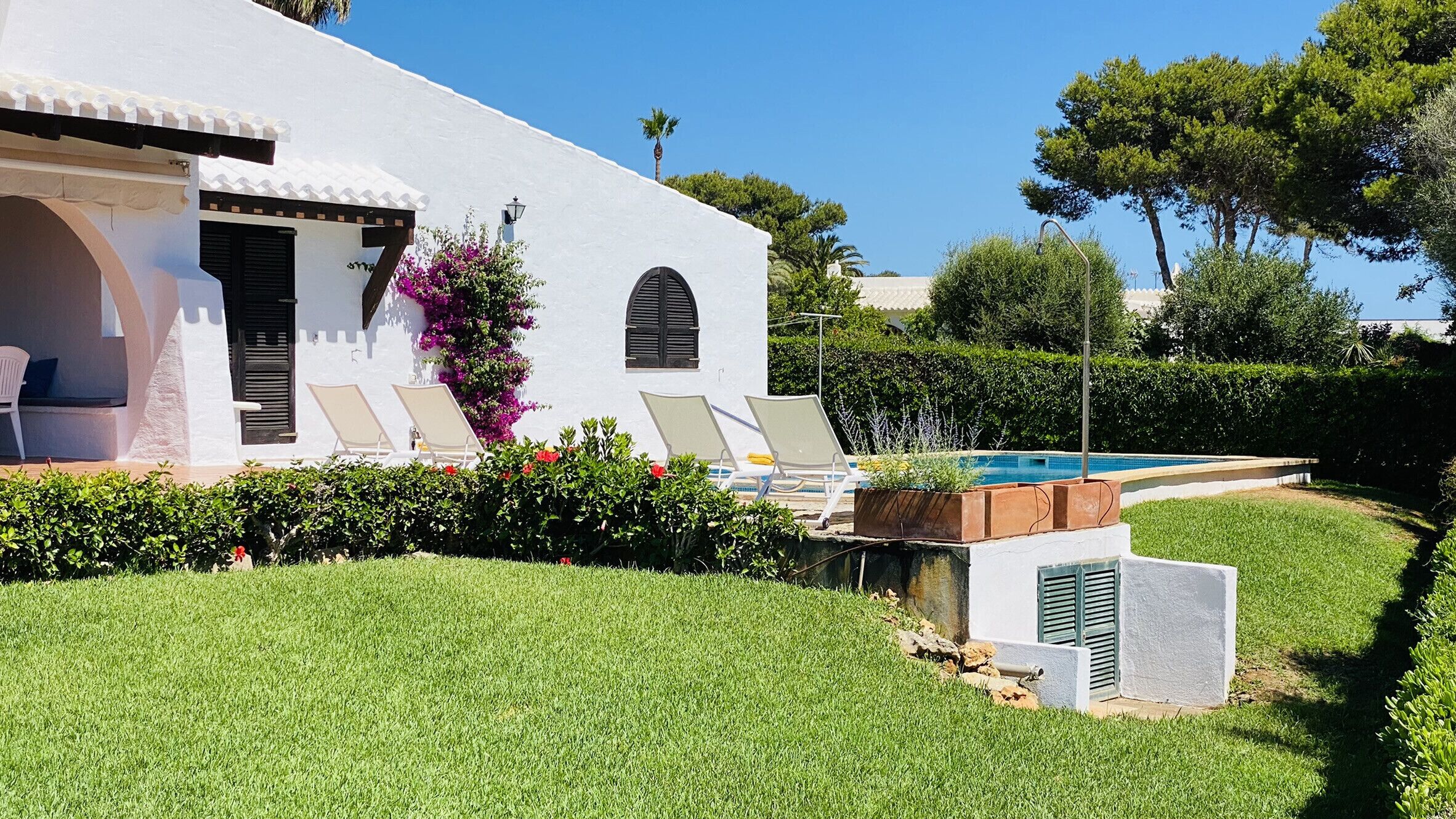 Una villa blanca con piscina, dos sillones de descanso y un pequeño jardín.