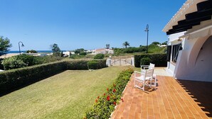 Eine Terrasse mit Meerblick, eine Rasenfläche und ein weißes Gebäude mit einem Ziegeldach.