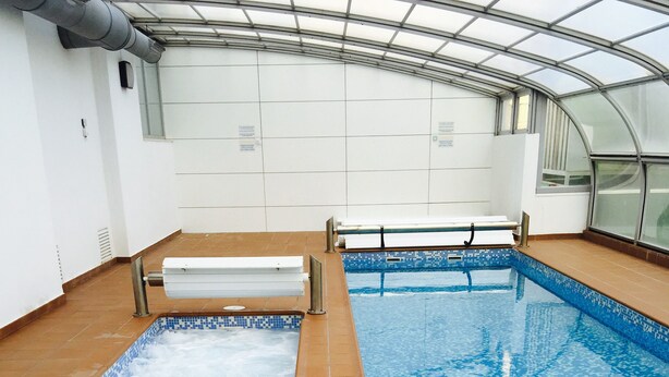 An indoor swimming pool with tiled floors and walls, a metal safety rail, and a glass ceiling. - BEAUTIFUL MEDITERRANEAN AVENUE APARTMENT (Benidorm)