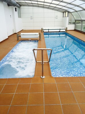 An indoor swimming pool with tiled floors and walls, a metal safety rail, and a glass ceiling. - BEAUTIFUL MEDITERRANEAN AVENUE APARTMENT (Benidorm)