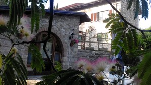A stone building with a wooden door and a window, surrounded by greenery and flowers.