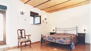 A bedroom with a bed, a chair, a nightstand, and a window.
