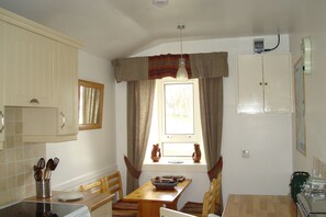 A small kitchen with a window, a dining table, and chairs. There are cabinets, a stove, and a sink.