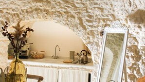 A kitchen with a stone wall, a sink, a mirror, and a vase with dried plants.