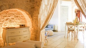 A cozy room with a stone wall, a white dresser with drawers, a bed with white bedding, and a table with chairs.