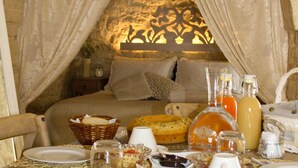 A cozy breakfast setup with a stone wall backdrop, a bed with a canopy, and a table with breakfast items and drinks.