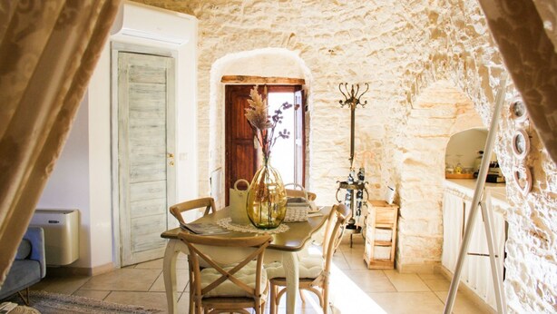 A rustic stone-walled room with a wooden dining table, chairs, and a small cabinet.
