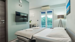 Ett modernt hotellrum med en säng, ett skrivbord, en stol, en TV och ett fönster med utsikt över grönområden.