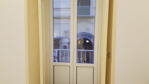 A door with a window, a balcony with a railing, and a building with an arched window in the background. - Apartment in the heart of Sorrento, 10 meters from Piazza Tasso (Sorrento)