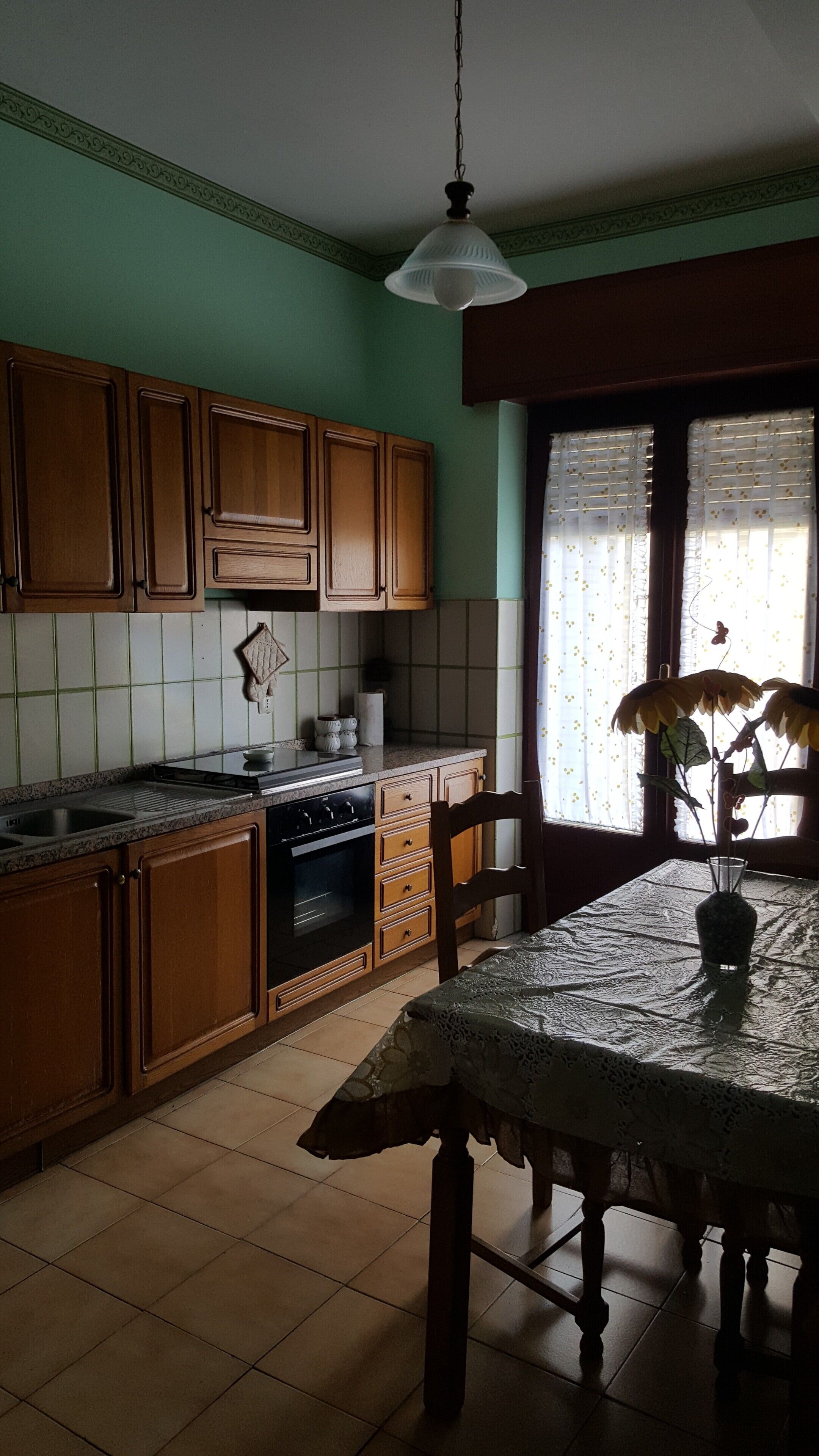 A kitchen with wooden cabinets, a stove, and a dining table with a vase.