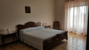 Una camera da letto con un letto di legno, un comodino con una lampada, una sedia e una finestra con tende.