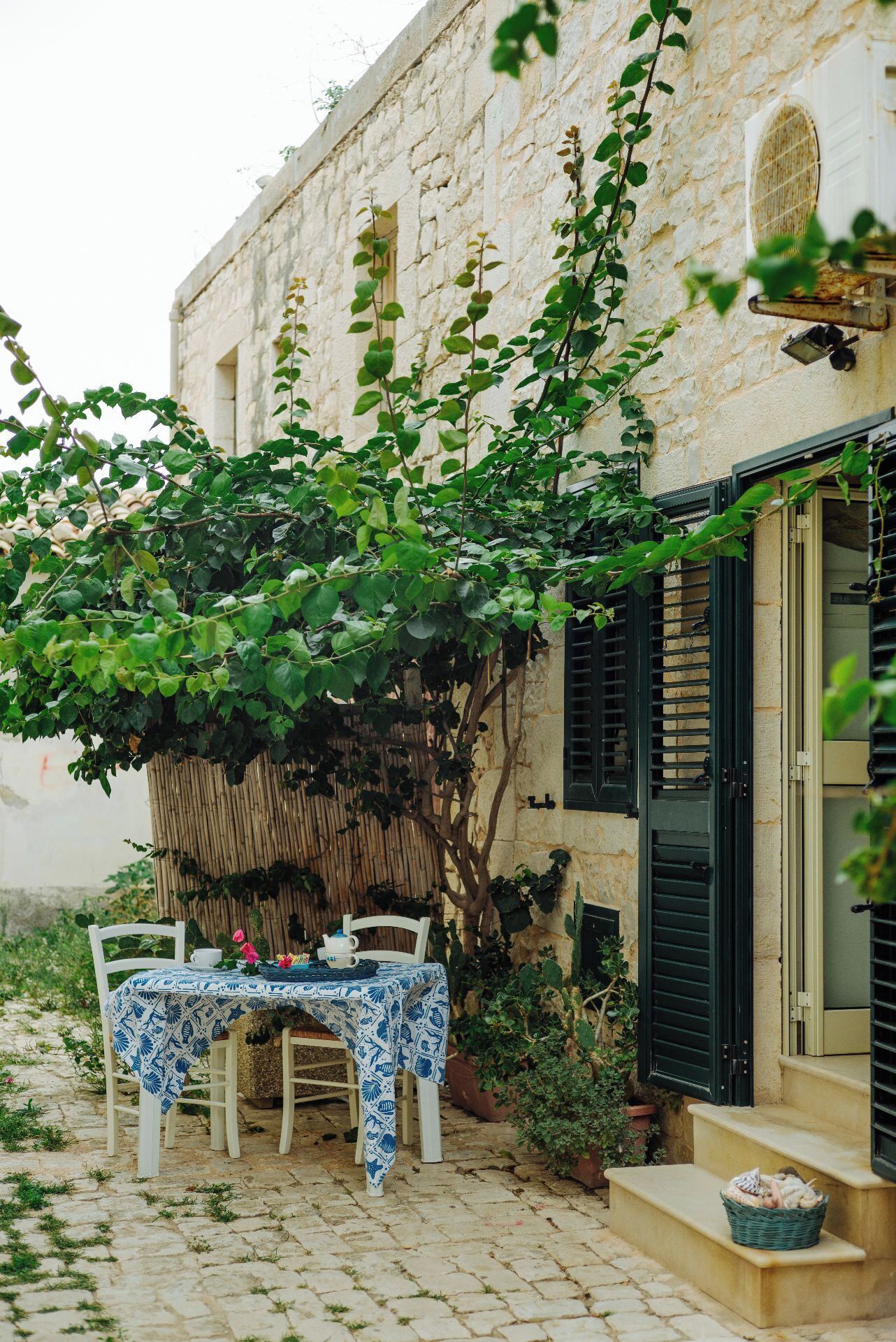 A stone building with a table set for two under a vine-covered pergola.