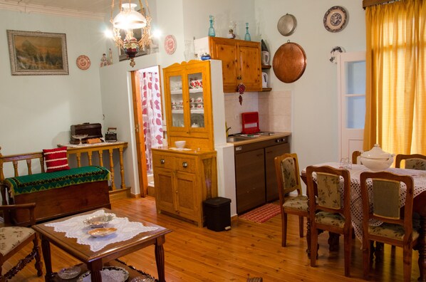 A traditional dining room with wooden furniture, a table set for four, and a kitchen area with cabinets and a sink. - THELGITRO, A Traditional House Located in the Heart of Skopelos Town (Skopelos town)
