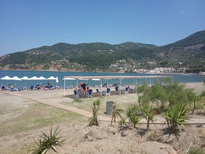 A beach with umbrellas and chairs, a clear view of the sea, and a hilly landscape in the background. - THELGITRO, A Traditional House Located in the Heart of Skopelos Town (Skopelos town)