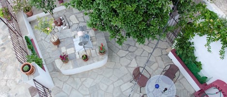 An outdoor patio area with stone flooring, a round table with chairs, potted plants, and a metal fence.