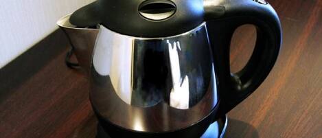 Una tetera eléctrica negra y plateada con un asa sobre una superficie de madera.