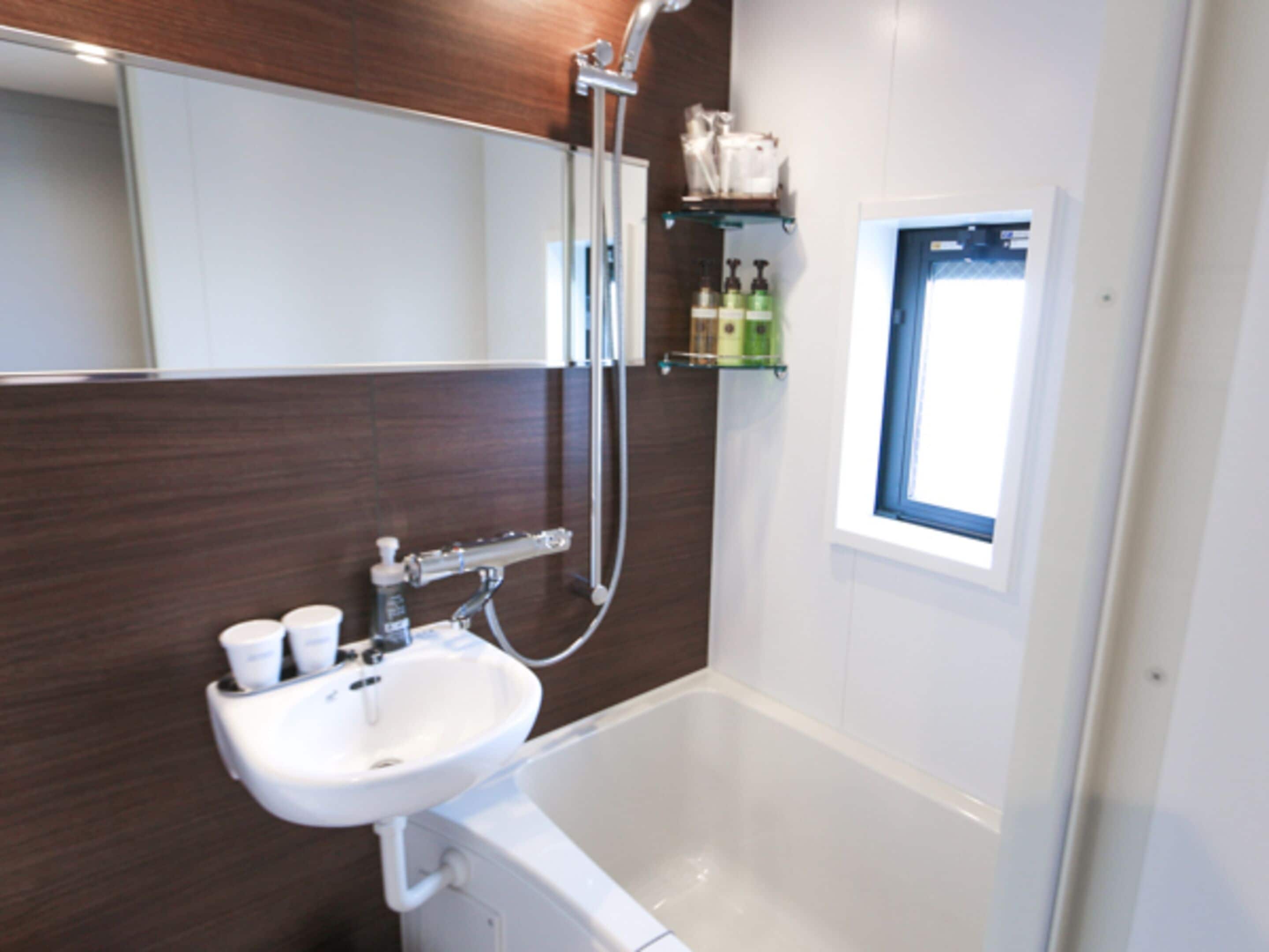 A modern bathroom with a white sink, a shower, and a window.