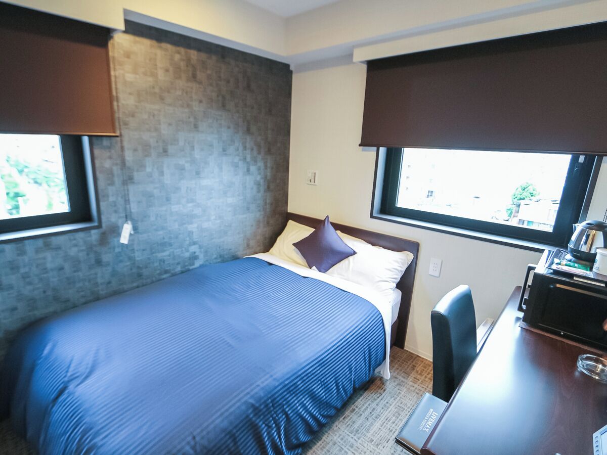 A hotel room with a bed, a desk, and a window.