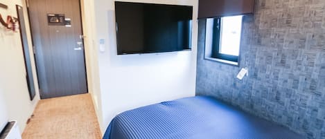 Habitación de hotel con cama, televisor de pantalla plana montado en la pared, equipo de aire acondicionado, ventana con vista y puerta.