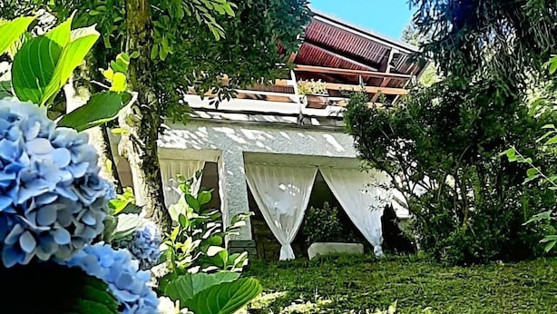 A garden with a gazebo, lush greenery, and a building with a red roof in the background.
