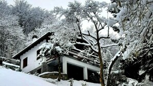A snow-covered landscape with a house, trees, and a wooden fence.
