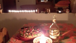 A dining table with a pizza, a candle, and a bottle.