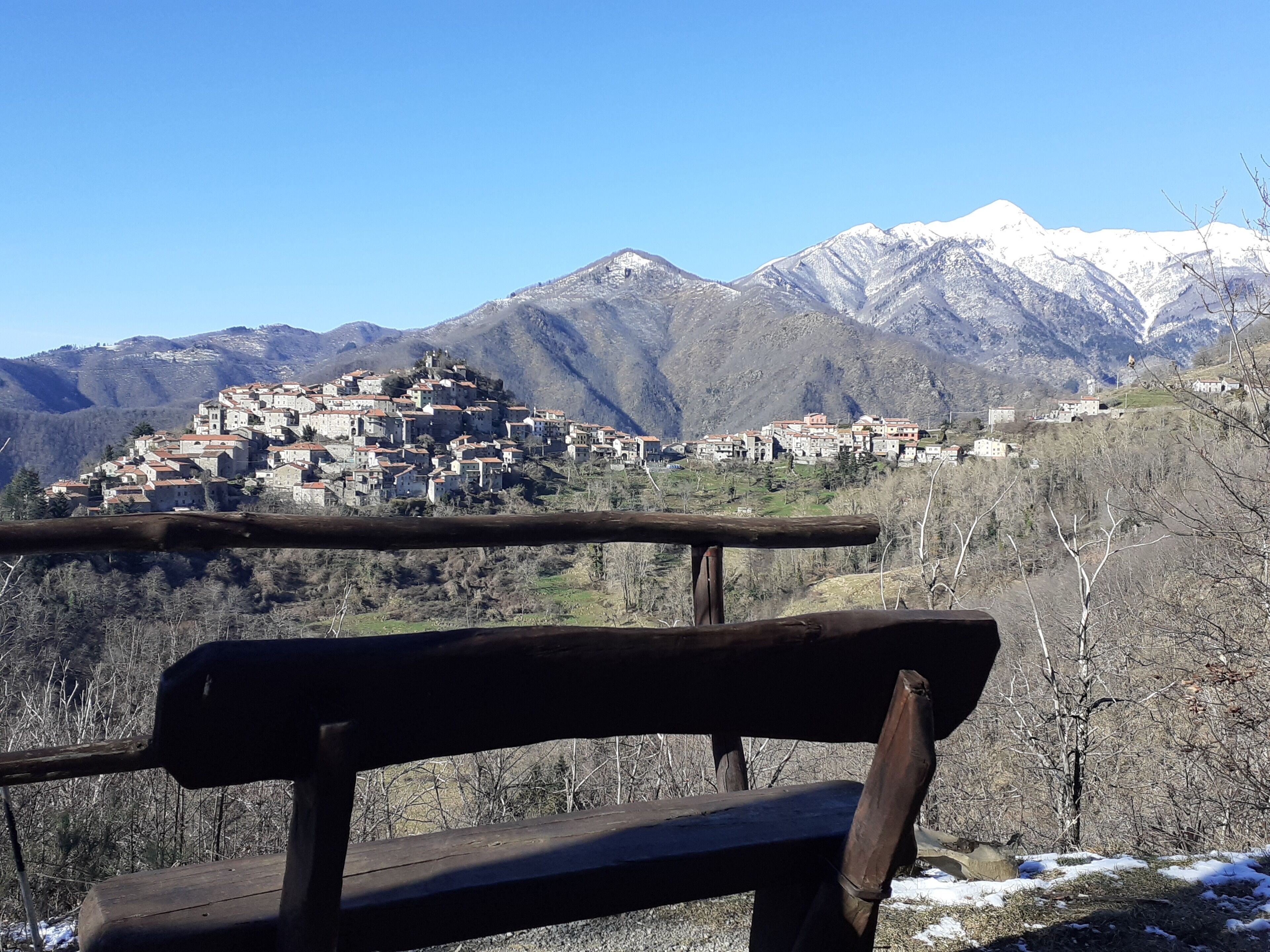 Un banco de madera con vistas a un pueblo montañoso y cumbres nevadas al fondo.
