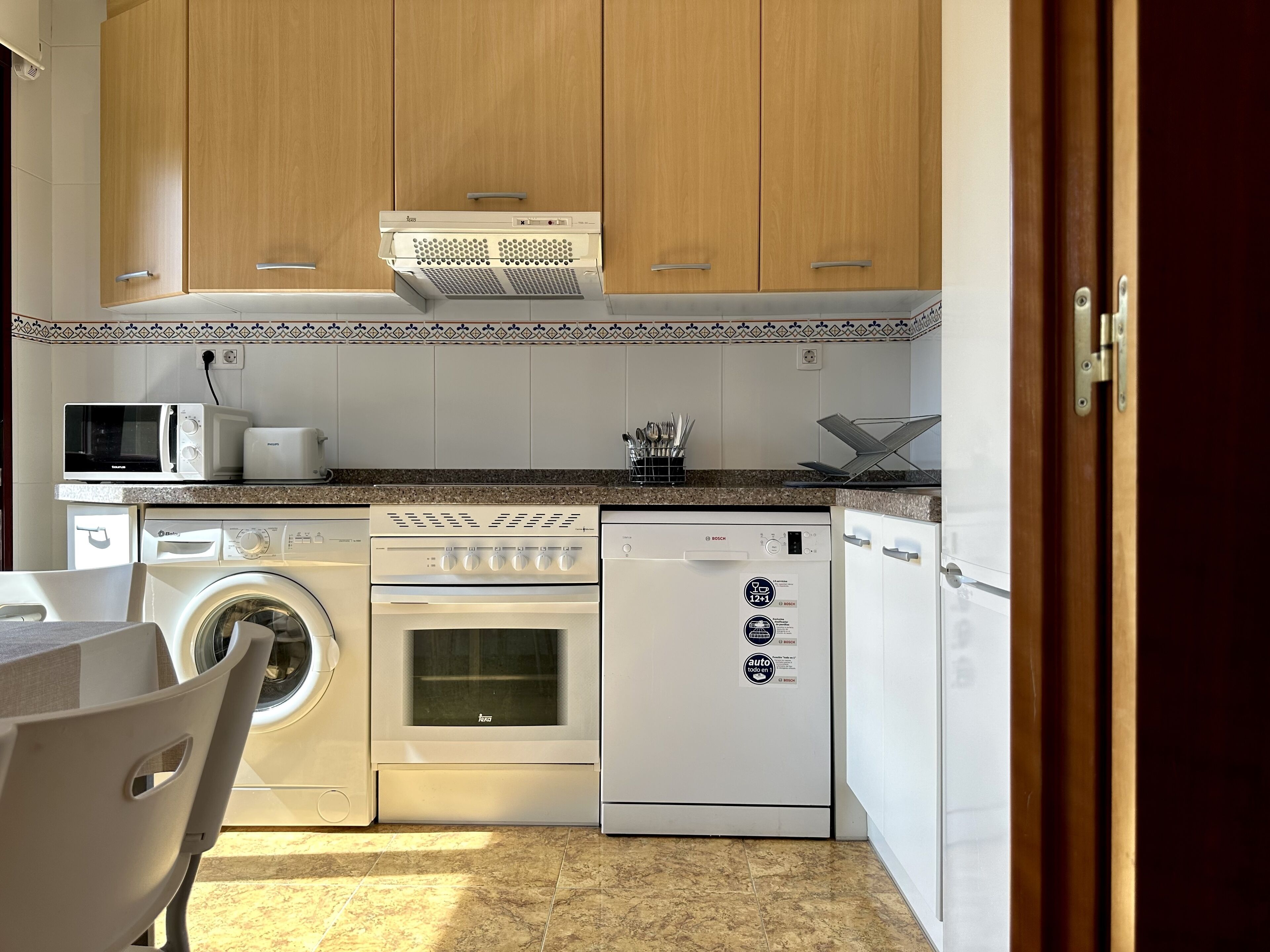 A compact kitchen with a washing machine, oven, and dishwasher.